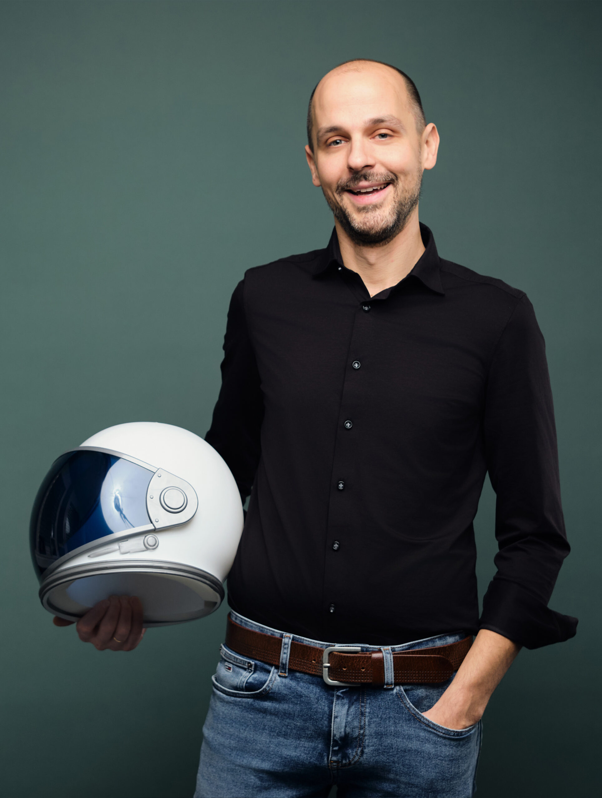 Ein Mann hält einen Astronautenhelm in der Hand und lächelt in die Kamera.