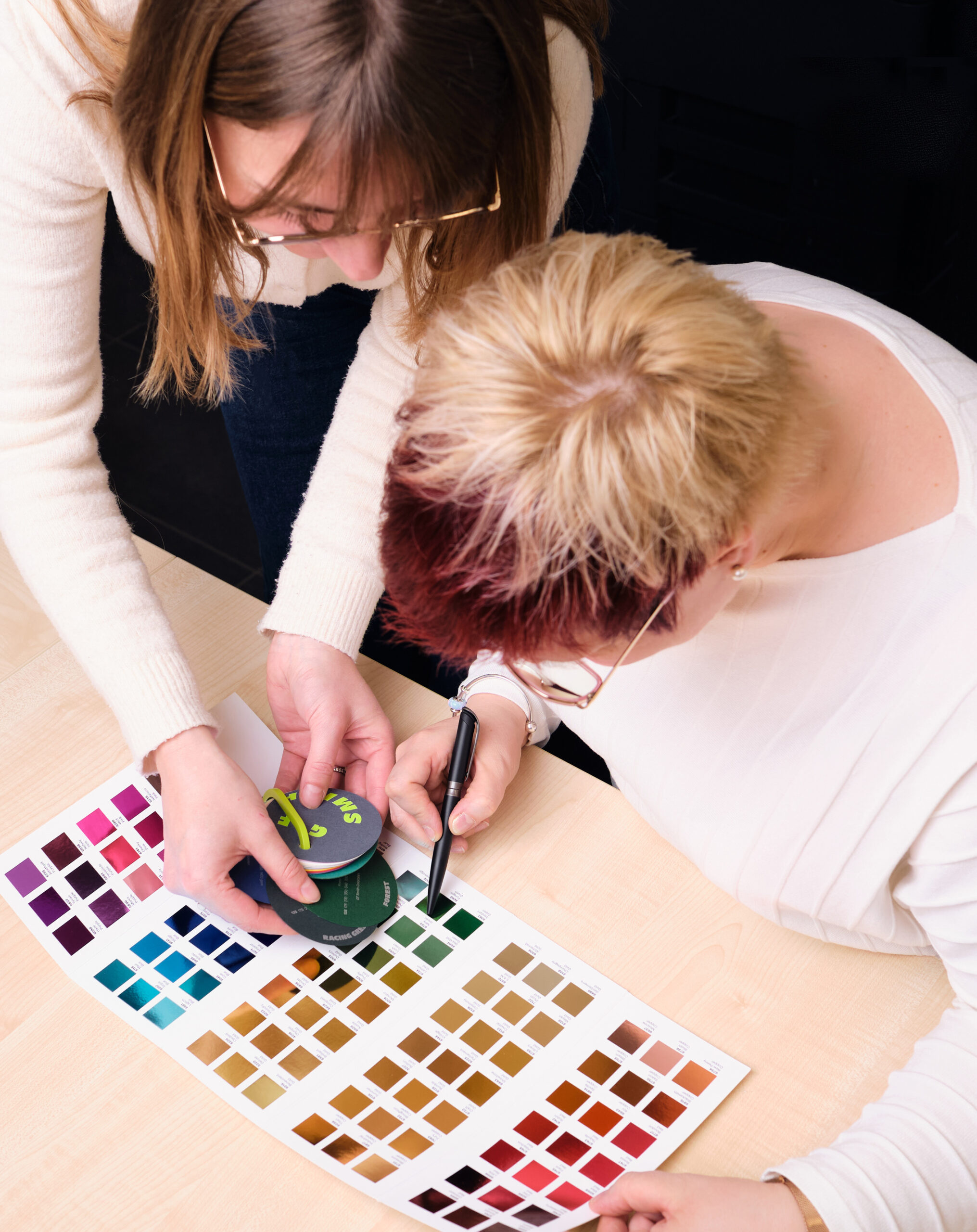 Zwei FRauen sind über einen Farbfächergebeugt und suchen eine passende Farbe aus.