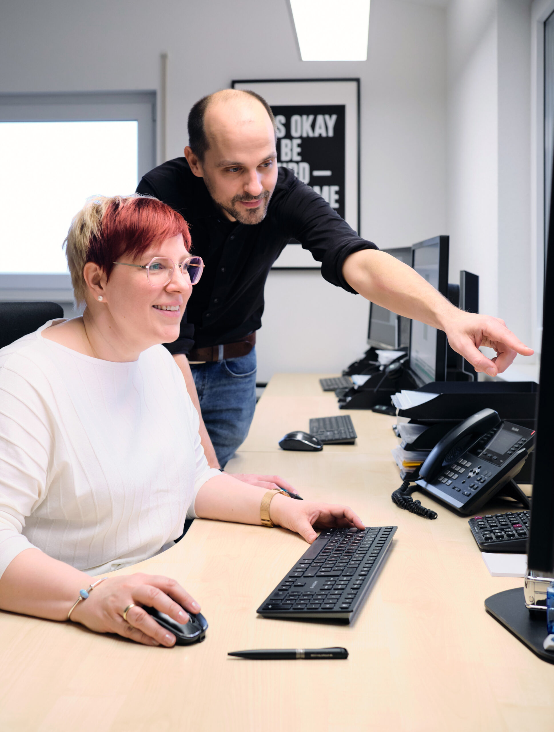 Zwei Menschen sitzen vor einem Bildschirm. Der eine deutet auf den Monitor.